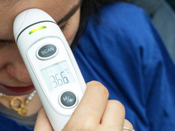 Eine Person hält das Fieberthermometer an die Stirn